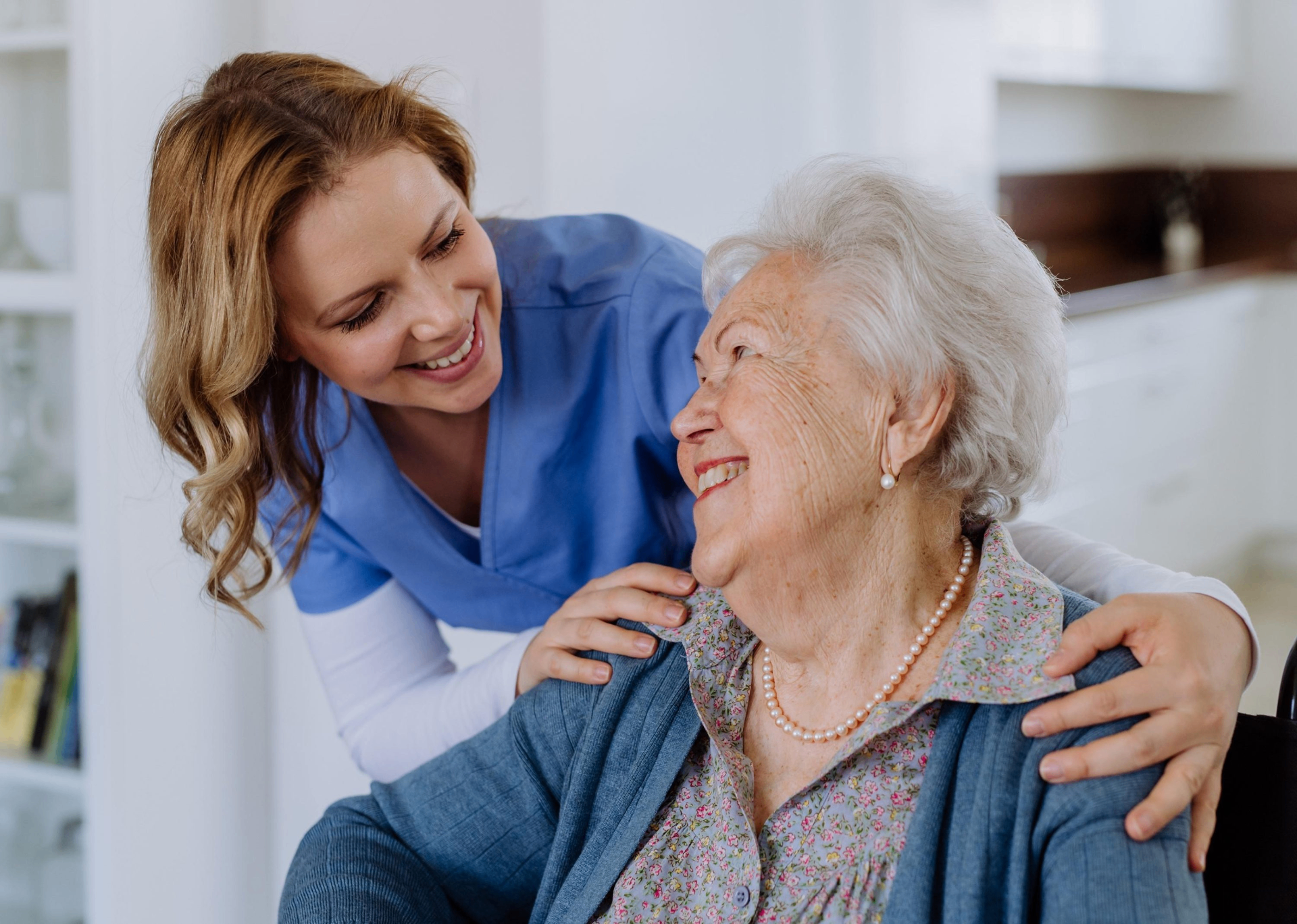 Caregiver in blue scrubs smiling warmly with an elderly woman